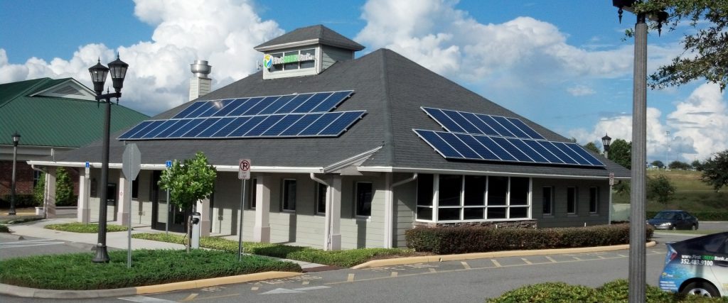 A building with solar panels on the roof under a partly cloudy sky.