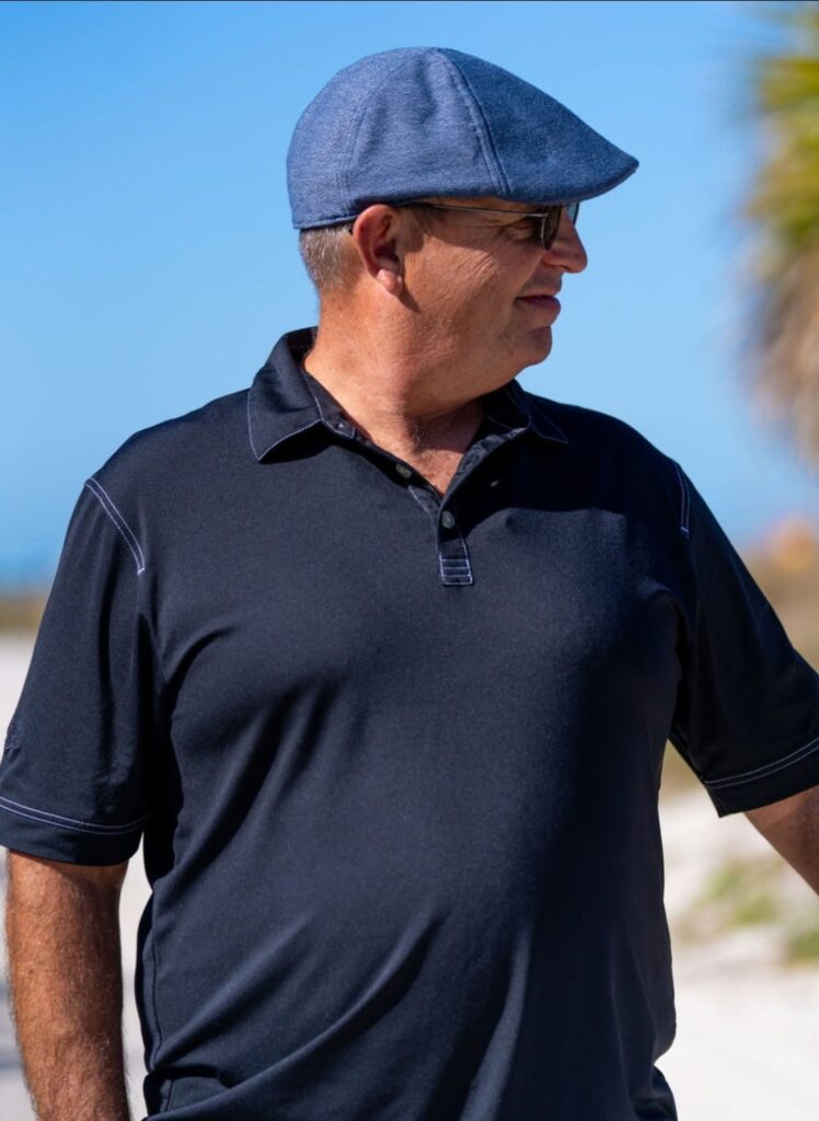 Man in a blue polo shirt and cap looking to the side outdoors.
